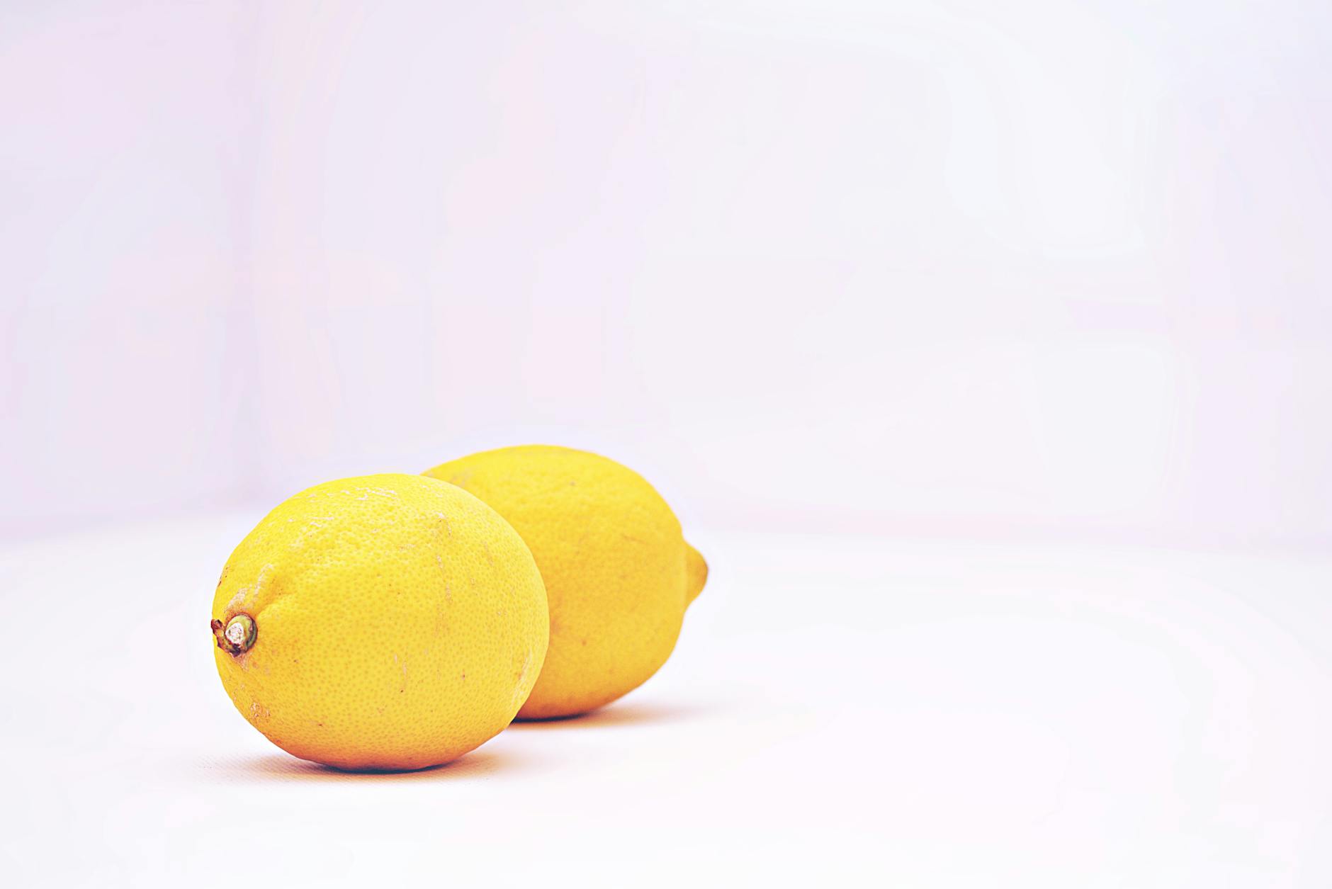 Hand holding a lemon on a soft pink background, representing the citrus-inspired design of lemon vibrators.