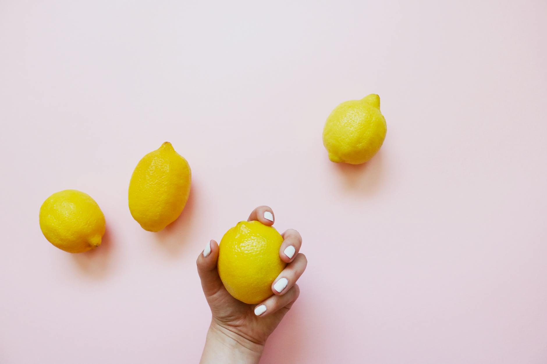 Hand holding a fresh lemon on a soft pink background, symbolizing natural body-safe choices