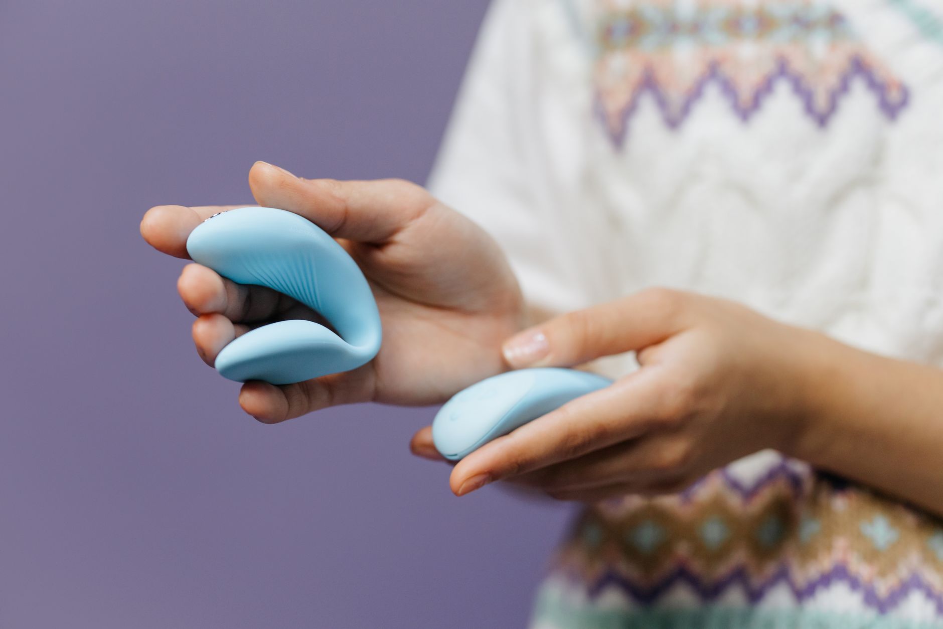 Close-up of a hand holding a vibrator against a purple background, emphasizing intimate connection