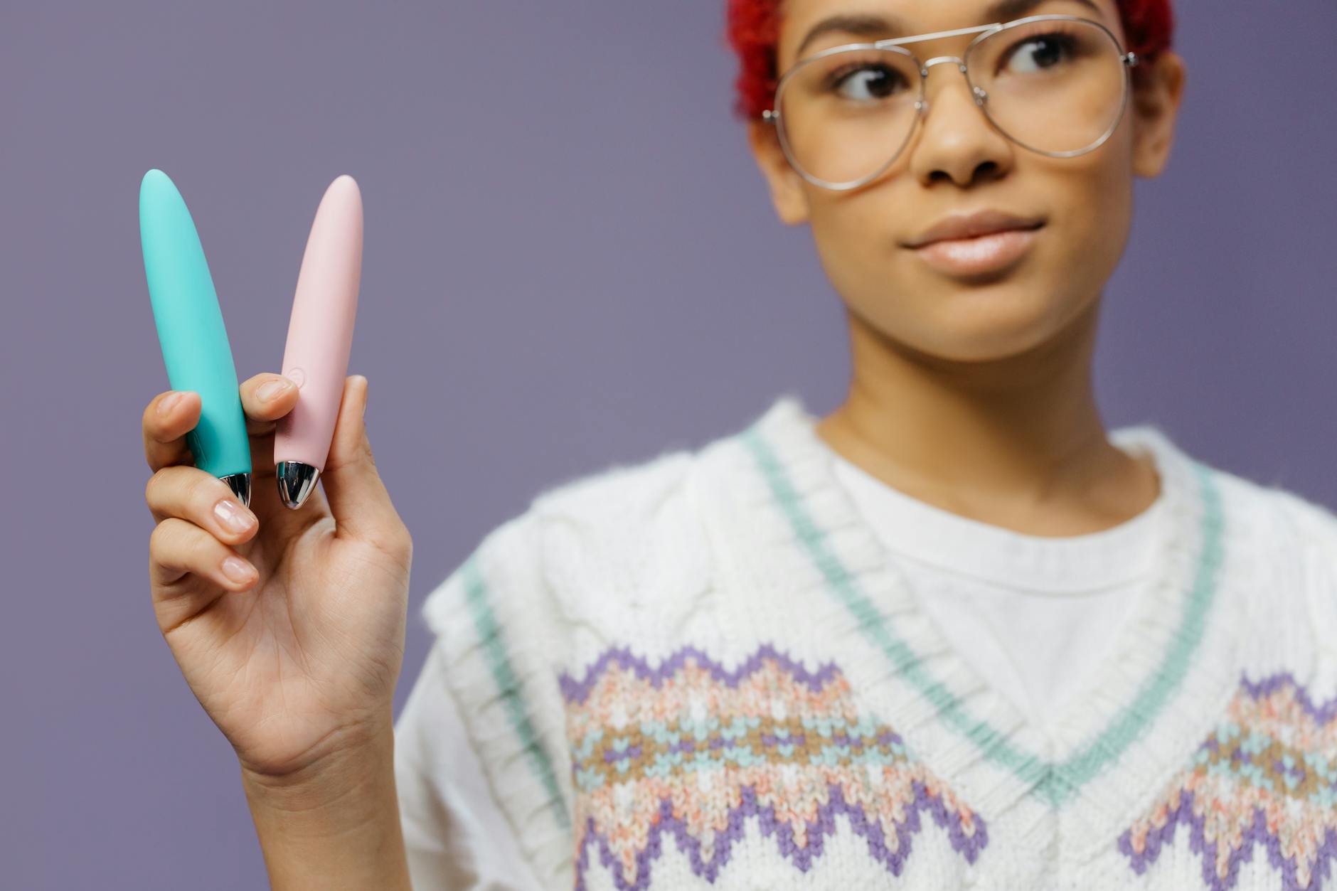 A young woman holds two vibrant clitoral vibrators against a purple background, representing pleasure and recovery options.
