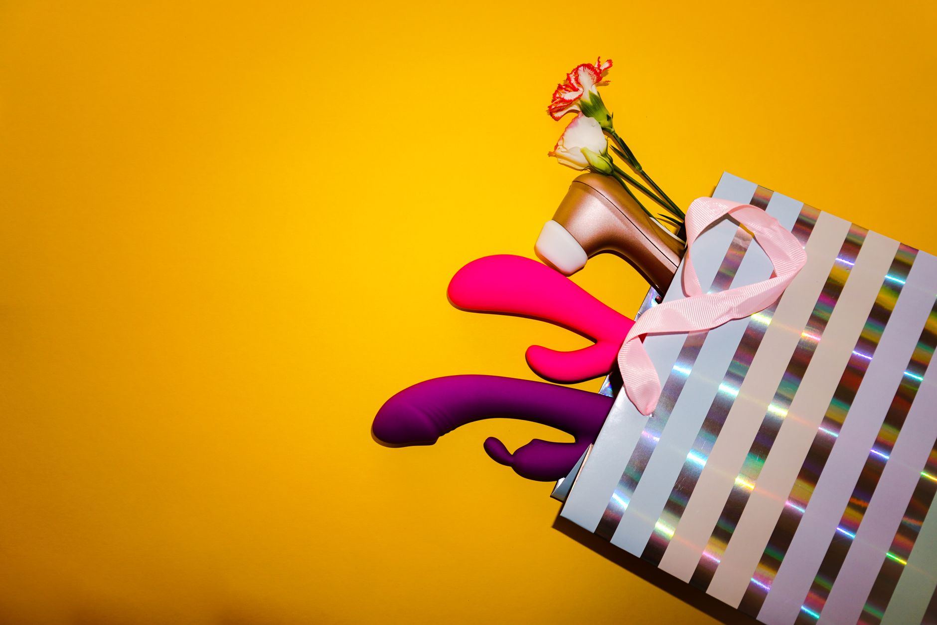 Colorful vibrators with flowers in a holistic gift display against a bold yellow background.